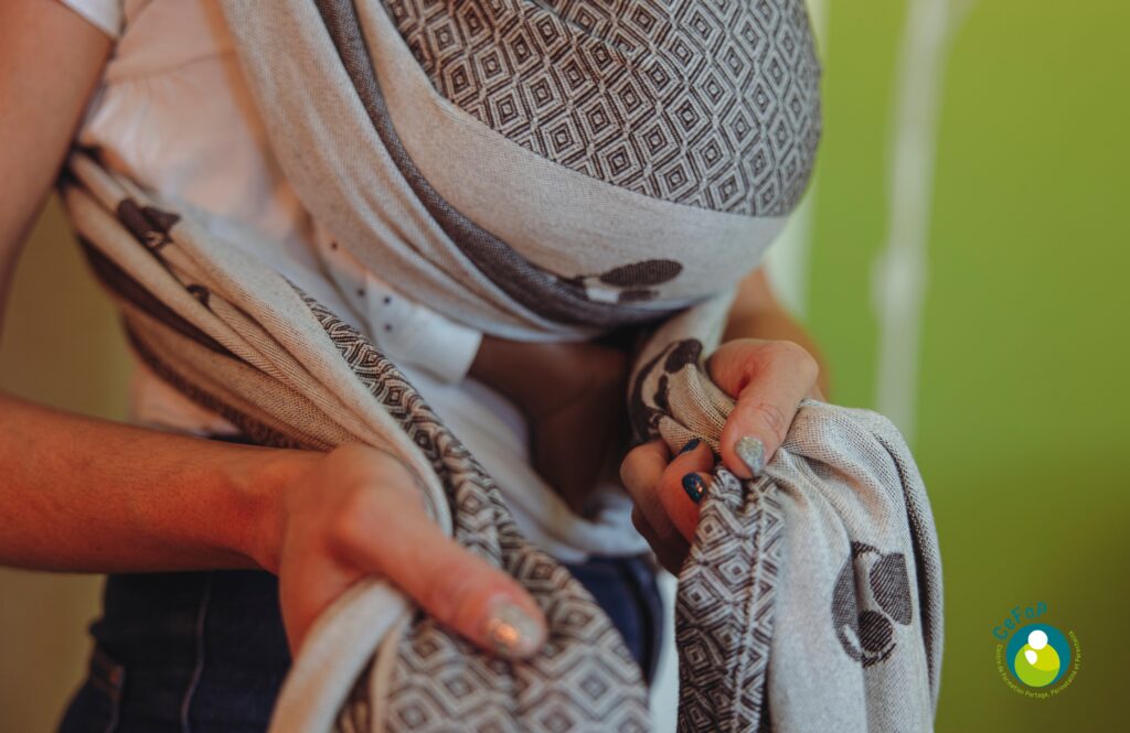 installation d'un poupon lesté dans une écharpe de portage pendant une formation au portage des bébés dans une crèche